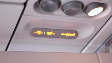 Uçak kabin kontrolleri kapalı. Aydınlatılmış emniyet kemeri ve sigara içilmediğini gösteriyor. Gösterişli panel tasarımı uçuş sırasında güvenlik talimatları ve yolcu bilincini vurguluyor