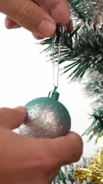 Dikey Mutlu Noeller ve mutlu tatiller. Bir adamın eli kışın evde ladin ağacını süslüyor. Dekorasyon afişi olarak köknar dallarının Noel baloları ve süslemeleri, yeni yıl konsepti.