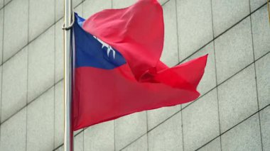 Tayvan ulusal bayrağının yavaş çekimleri modern bir binanın arka planına doğru dalgalanıyor. Odaklanan bayrak, açık mavi ve kırmızı bir tasarımla vatanseverlik gururu ve kültürel önemini gösteriyor..