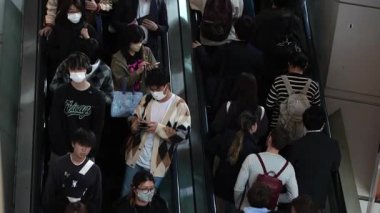 Tokyo, Japonya-10 Nisan 2023: Bir grup Asyalı alışveriş merkezinin yürüyen merdivenlerine biniyor, Japon müşteriler alışveriş çılgınlıkları için yoğun saatlerde hareket halindeki merdivenleri kullanıyorlar..