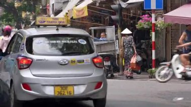 Hanoi, Vietnam-04 Nisan 2024: Vietnamlı bir kadın Hanoi Eski Mahallesi 'nde bir cadde boyunca yürüyor, geleneksel Asya konik hasır şapkası takıyor, Vietnam kültür mirasının simgesi..