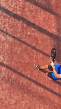 Dikey olarak, dışarıda tenis oynayan bir adamın topa vuruşunun üst görüntüsü..