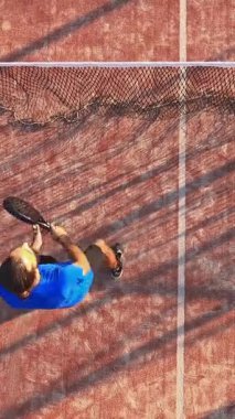 Dikey olarak, dışarıda bir sahada raket tenisi oynayan bir adamın görüntüsü..