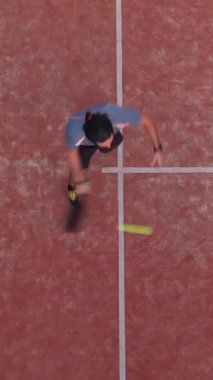 Dikey, dış sahada maç yapan bir raket tenisçisinin yukarıdan görüntüsü.