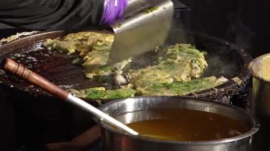 Tayvan 'ın Taichung kentindeki gece pazarından spatulayla istiridye omleti aşıran bir satıcının ağır çekimde.