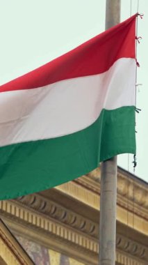 Budapeşte 'deki tarihi bir binaya hafifçe sallanan Macar bayrağının dikey yavaş hareketi. Miras mimarisinin arka planına karşı kurulan güçlü bir ulusal gurur sahnesi.
