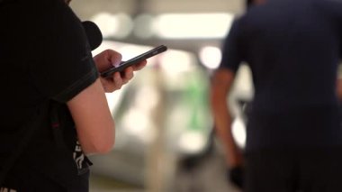 Modern havaalanının terminalinde akıllı telefonu tutan eller. Yoğun bir ulaşım merkezinde seyahat ve bağlantının mükemmel bir tasviri. Teknoloji ve seyahat içeriği için kullanışlı.