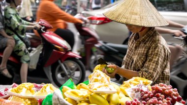 Hanoi, Vietnam-04 Nisan 2024: Geleneksel Asya konik hasır şapkası takmış Vietnamlı bir sokak satıcısı, bisikletini Hanoi, Vietnam 'da bir yol boyunca mobil meyve tezgahı olarak kullanıyor..