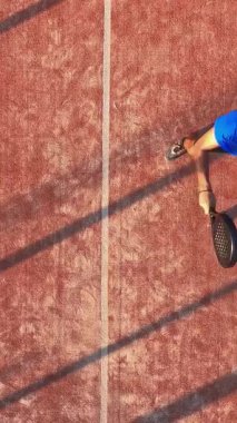 Açık havada tenis oynayan bir adamın dikey, üstten çekimi. Padel yarışmasına hazırlanıyor..