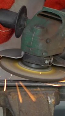 Worker in special clothes and gloves grinding metal with a circular saw in his workshop, bright sparks of metalworking fly in different directions.