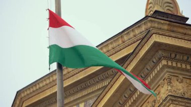 Budapeşte 'deki tarihi bir binanın yanında yavaşça dalgalanan Macar bayrağı, ülkenin mimari mirasını ve gururunu simgeliyor..