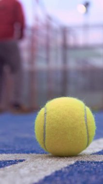 Açık havada mavi kortta Padel Ağı 'nın arkasında yerde sarı top var. Kürek tenisi oynayan adam. Beyaz tenli bir sporcu topa vuruyor. Raket sporu kavramı.