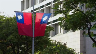 Kentsel bir ortamda sokak lambası direğine asılı ikiz Tayvan bayrakları. Şehir yaşamının ve yeşilliğin arka planına karşı milli gurur sembolü..