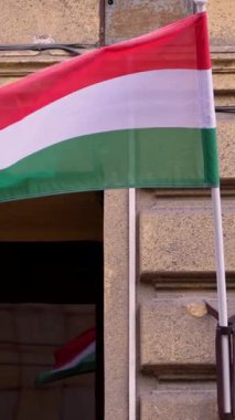 Güneşli Budapeşte gökyüzünde zarif bir şekilde dalgalanan Macar bayrağının dikey yavaş çekimi. Ulusal gurur, kültür ve sükuneti harekete geçiren bir an.