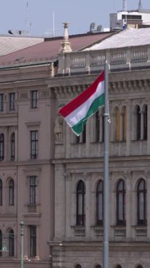 Budapeşte 'deki Macar bayrağının dikey yavaş çekim görüntüsü, tarihi mimariye karşı zarafetle akıyor. Kültürel gurur ve ulusal kimliğin simgesi..