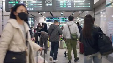 Taipei, Tayvan-07 Mart 2025: Kalabalık tren istasyonunun içinde farklı yönlere yürüyen, yoğun saatlerde yolcu tahtalarının altından geçerken çantalar ve sırt çantaları taşıyan insanlar..