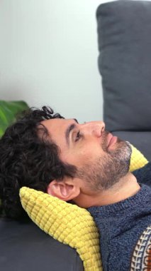 Akıllı telefonunu kullanarak gülümseyen ve evdeki kanepede uzanan mutlu yakışıklı adam. Kendine güveni tam sakallı bir adam. Evdeki koltukta rahatlıyor ve daktilo kullanıyor..