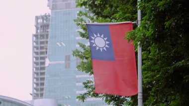 Arka planda yeşil bir ağaç ve şehir binası olan Tayvan bayrağının yavaş çekimleri, doğayı kentsel gururla birleştiriyor. Çevresel ve kültürel temalar için ideal.