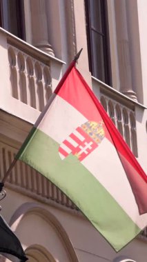 Macar bayrağının dikey yavaş hareketi Budapeşte 'deki süslü bir binaya karşı zarafetle dalgalanıyor. Şehirdeki ulusal gurur ve mimari güzelliği yakalıyor..