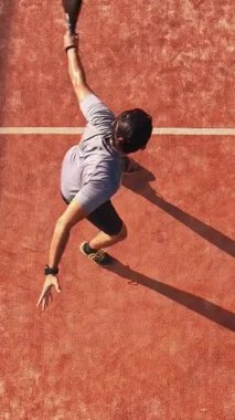 Açık havada raket oynayan bir adamın dikey ve üst görüntüsü. Devamlı raketle topa vuruyor..