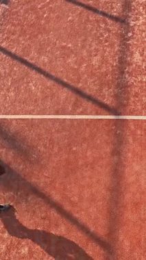 Dış sahadaki bir yarışmaya katılmak için raket tenis antrenmanı yapan genç bir adamın dikey ve üst görüntüsü.