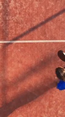 Dış sahadaki bir spor antrenmanı sırasında ayakta duran ve topa vuran profesyonel bir Padel oyuncusunun dikey ve tepeden çekimi..
