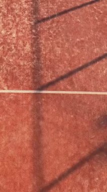 Dikey olarak, bir padel oyuncusunun yukarıdan görünüşü hızla topa vuruyor ve açık sahadaki bir maçta internete gidiyor..