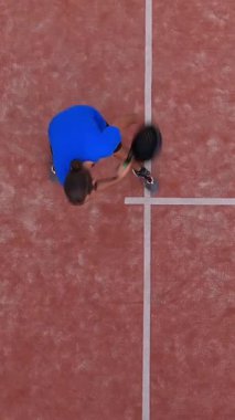 Dikey, dış sahada çalışan bir raket tenisçisinin yukarıdan görüntüsü.