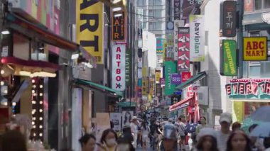 Güney Kore, Seul - 10 Temmuz 2025: Myeongdong 'da dar renkli yolda ilerleyen yayaların yavaş çekimleri, dükkanlar, dikey afişler ve öğleden sonra alışveriş saatleri boyunca hareketli aktiviteler