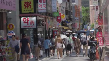 Güney Kore, Seul - 10 Temmuz 2025: Kalabalık Myeongdong caddesinde insanlar alışveriş yaparken, bazıları renkli dükkanlar, sokak yemekleri ve kentsel ortam ile çevrili şemsiyeler taşırken,