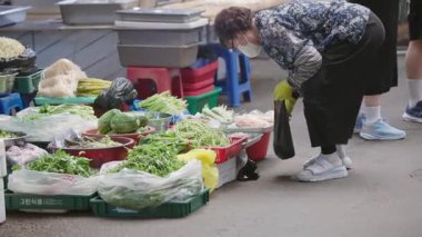 Güney Kore, Seul - 09 Temmuz 2025: Gwangjang Market Caddesi 'ndeki tezgahta sergilenen rengarenk taze sebzelerin yavaş çekimleri yaz öğleden sonra geçmekte olan yerel yolcular.