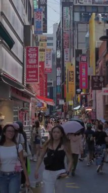 Güney Kore, Seul - 10 Temmuz 2025: Myeongdongs 'un orta kesiminde turizm, alışveriş kültürü ve hareketli tabelaları gösteren renkli ticari caddelerde yürüyen ağır çekim dikey kalabalık