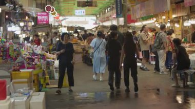 Güney Kore, Seul - 09 Temmuz 2025: Gwangjang Market, Seul 'deki dar gıda aralığının görüntüsü yavaş çekim, yerli halk ve ziyaretçiler parlak ışık altında yiyecek satın alıyorlar