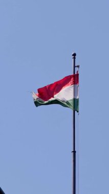 Budapeşte 'nin mavi gökyüzüne karşı bir direğin üzerinde dalgalanan Macar bayrağının dikey yavaş çekimi. Ağır çekimde vatansever bir gurur ve kültürel kimlik sahnesi.