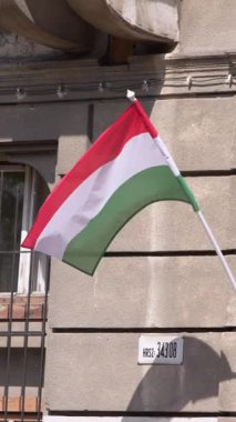 Budapeşte 'deki Macar bayrağının dikey yavaş çekim görüntüsü, tarihi mimariye karşı zarafetle akıyor. Kültürel gurur ve ulusal kimliğin simgesi..