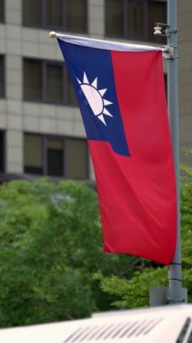 Modern bir binanın yakınında dalgalanan tek bir Tayvan bayrağının dikey yavaş hareketi, Tayvan kimliğini temsil ediyor..