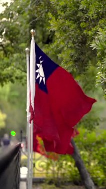 Tayvan bayrağının dikey olarak yavaşça dalgalanan hareketi huzurlu bir park ortamında ağaçlar arasında ulusal gururu doğal bir ortamda yakalıyor..