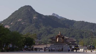 Güney Kore, Seul - 10 Temmuz 2025: Güneşli bir yaz sabahı, Güney Kore şehir merkezindeki dağ ve geleneksel saray binaları tarafından çerçevelenmiş Kral Sejong heykelinin geniş bir görüntüsü