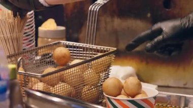 Myeongdong gece pazarında sıcak kabin ışığı altında gevrek atıştırmalıkları kağıt bardaklara dolduran Koreli satıcının yavaş çekim yakın çekimi dokuyu ve hareketi vurguluyor..