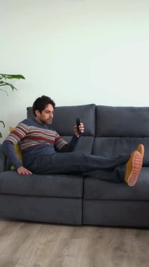 Neşeli yakışıklı adam evdeki kanepede uzanırken akıllı telefonunu kullanıyor. Kendine güveni tam sakallı adam akıllı telefonuyla evin kanepesinde daktilo çekiyor..
