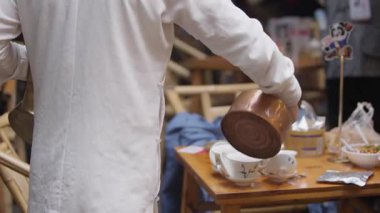 Chengdu, Çin-11 Ekim 2024: Chengdu 'daki ahşap masada uzun soluklu çaydanlık ile geleneksel çay seremonisinin yavaş çekimleri, rafine edilmiş Çin servis ritüelini sergiliyor.