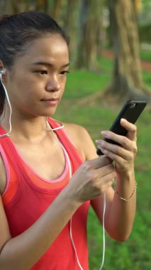 Genç Asyalı kadın koşucu Daan Park Taipe şehrinde koşuya hazırlanıyor, kulaklıklarını takıyor. Güzel güneşli bir yaz günü Tayvan. Egzersiz Konsepti. Spor yaşam tarzı. Kaydırma Kamerası Hareketi