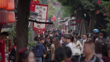 Chengdu, Çin-11 Ekim 2024: Chengdus kırmızı fener sokağında yürüyen insanların yavaş çekim akışı, yukarıdan çekilen sinematik derinlik ve şenlikli şehir enerjisiyle