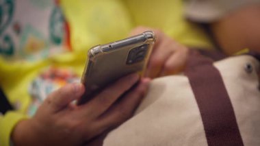 Taipei metro vagonunda akıllı telefondan mesajlaşan, parlak sarı arka planlı, yavaş çekim yakın çekim eller.