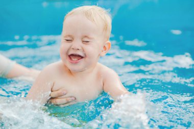Kızıl saçlı küçük bir çocuğun portresi bahçede açık havuzda el desteği ile yıkanır, bebek suda oynar, yaz tatili yapar.