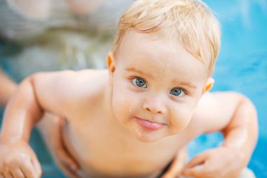 Kızıl saçlı küçük bir çocuğun portresi bahçede açık havuzda el desteği ile yıkanır, bebek suda oynar, yaz tatili yapar.