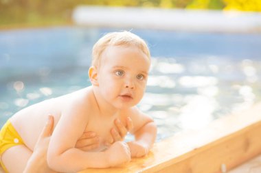 Kızıl saçlı küçük bir çocuğun portresi bahçede açık havuzda el desteği ile yıkanır, bebek suda oynar, yaz tatili yapar.