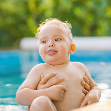 Kızıl saçlı küçük bir çocuğun portresi bahçede açık havuzda el desteği ile yıkanır, bebek suda oynar, yaz tatili yapar.