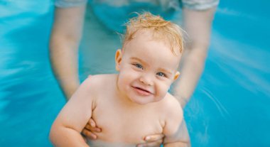 Kızıl saçlı küçük bir çocuğun portresi bahçede açık havuzda el desteği ile yıkanır, bebek suda oynar, yaz tatili yapar.