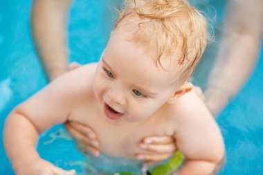 Kızıl saçlı küçük bir çocuğun portresi bahçede açık havuzda el desteği ile yıkanır, bebek suda oynar, yaz tatili yapar.